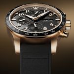 IWC Pilots Watch in Rotgold mit schwarzer Luenette, Zifferblatt und Kautschukarmband vor braungold-schwarzem Hintergrund