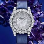 Chopard L'Heure du Diamant Damenuhr mit Gehaeuse in Weissgold besetzt mit Diamanten, silbernem Zifferblatt mit roemischen Ziffern und blauem Textilarmband vor blauem Hintergrund