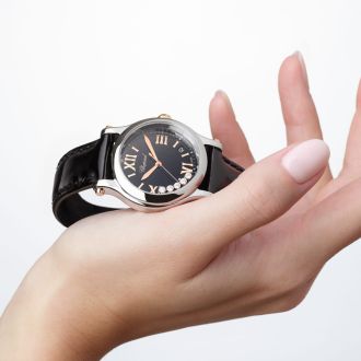 Damenhand haelt eine Happy Sport Uhr von Chopard in Stahl mit schwarzem Zifferblatt mit fuenf beweglichen Diamanten und schwarzem Lederarmband