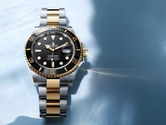 Rolex Submariner Date Rolesor Stahl-Gold mit schwarzer L&uuml;nette vor blauem Meereshintergrund mit Wasserreflexionen