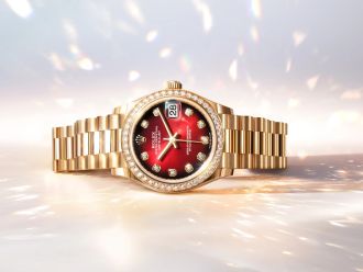 Rolex Datejust aus Gelbgold mit rotem Ombré-Zifferblatt und diamantbesetzter Lünette auf hellem, funkelndem Hintergrund.