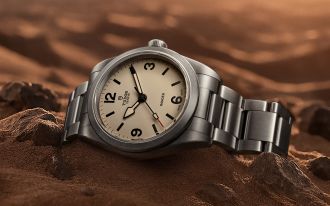 Edelstahl-Armbanduhr Tudor Ranger mit cremefarbenem Zifferblatt auf sandig-felsigem Untergrund.