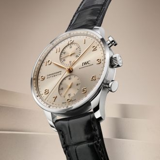 IWC Portugieser Chronograph in Stahl mit sandfarbenem Zifferblatt und schwarzem Lederarmband vor sandfarbenem Hintergrund