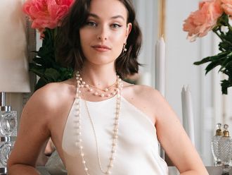 Frau in cremefarbenem Seidentop trägt mehrere elegante Perlenketten von Yana Nesper, im Hintergrund Blumen und Kerzen in stilvollem Ambiente.