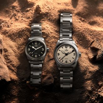 Zwei TUDOR-Ranger Modelle auf sandigem Untergrund – links die neue 36-mm-Ausführung, rechts die 39-mm-Version mit dem neuen Zifferblatt in „Dust“, beide mit Edelstahlband.