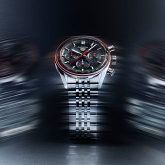 TAG Heuer Carrera Chronograph aus Edelstahl mit schwarzem Zifferblatt, roten Akzenten und Metallarmband, frontal dargestellt vor dynamisch verschwommenem Hintergrund.