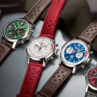 Vier Breitling Top Time Chronographen mit Stahlgehaeusen, unterschiedlich farbigen Zifferblaettern, gruen, weiss, blau und rot und Lederarmbaender liegend auf Lifestylehintergrund