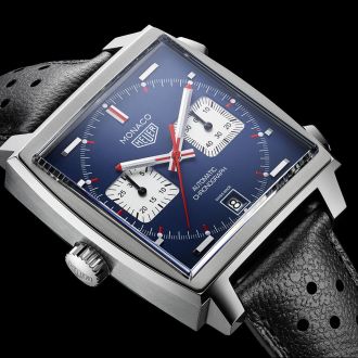 Maennliches Model traegt eine Monaco Uhr von TAG Heuer in Stahl mit blauem Zifferblatt, Krone bei 9 Uhr und Chronographendruecker bei 2 und 4 Uhr
