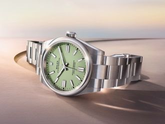 Rolex Oyster Perpetual in Stahl mit gruenem Zifferblatt seitlich auf braunem Untergrund liegend