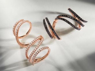 Zwei Crivelli Vortice Spiralenringe aus Roségold, einer mit weißen, einer mit schwarzen Diamanten, auf hellem Hintergrund.