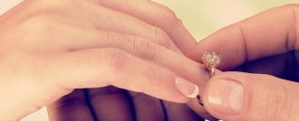 Person steckt Partnerin einen Diamant-Verlobungsring mit Krappenfassung an den Finger &ndash; Antragsszene mit klassischem Solit&auml;r