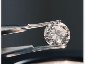 Lose gehaltener runder Diamant im Brillantschliff in einer Pinzette bei der Qualitätsprüfung