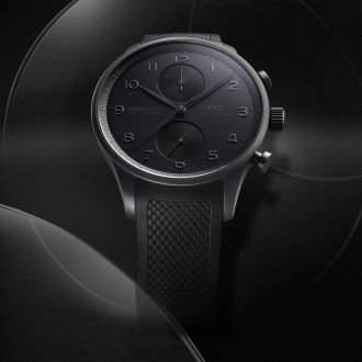 IWC Portugieser Chronograph Ceratanium mit schwarzem Zifferblatt, arabischen Ziffern und schwarzem strukturiertem Armband, elegante Luxus-Armbanduhr vor dunklem Hintergrund.