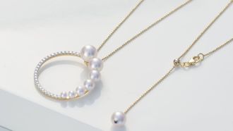 Goldene Kette von Yana Nesper mit weißen Perlen und rundem Anhänger auf weißer Fläche.