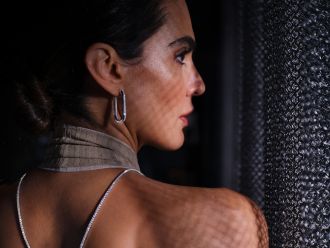 Frau mit eleganten silbernen Creolen und Halskette aus dem Atelier Mühlbacher, im Profil vor strukturierter Wand.