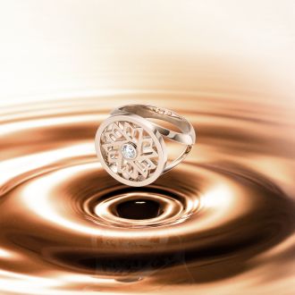 Luxuriöser Roségold-Ring von Danuvina by Mühlbacher mit feinem, offen gearbeitetem Design und Diamant in der Mitte, präsentiert auf einer fließenden, goldschimmernden Oberfläche.
