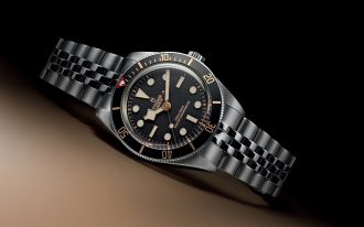 Tudor Black Bay Taucheruhr in Edelstahl mit schwarzem Zifferblatt und L&uuml;nette, goldfarbenen Akzenten und Metallarmband, stilvoll inszeniert auf dunklem Hintergrund