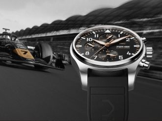 Formel-1-Rennwagen mit der Startnummer 7 fährt auf einer Rennstrecke; rechts groß im Vordergrund eine IWC Schaffhausen Pilotenuhr mit schwarzem Zifferblatt und Chronographenfunktionen