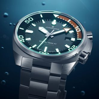 Junghans Aquaris Diver Taucheruhr aus Edelstahl mit dunkelgrauem Zifferblatt, Leuchtindizes, innenliegendem Drehring und Datumsanzeige vor Unterwasser-Hintergrund.