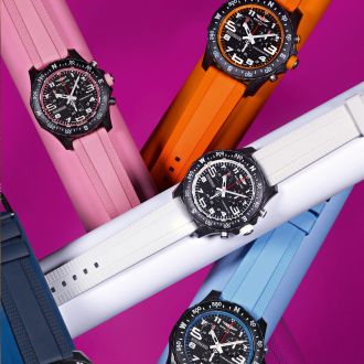 Vier Breitling Professional Uhren mit schwarzen Breitlight-Gehaeusen, schwarzen Zifferblaettern und farbigen Kautschukbaender, rosa, orange, weiss und hellblau auf pinkem Hintergrund