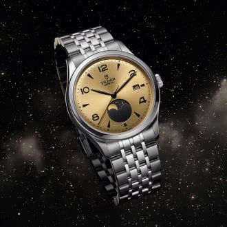 Produktaufnahme der TUDOR 1926 Luna mit champagnerfarbenem Zifferblatt, schwarzer Mondphasenanzeige und Edelstahlarmband vor Sternenhimmel.