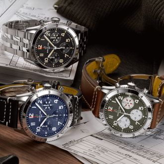 Drei Breitling Classic AVI Chronographen mit Stahlgehaeuse, Zifferblaetter in schwarz, blau, militarygruen und Stahl- und Lederarmbaender auf Lifestylehintergrund