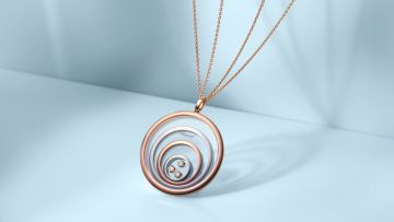 Chopard Happy Spirit Anhaenger aus mehreren Kreisen in Rose- und Weissgold, im innersten Kreis drei bewegliche Diamanten, an einer feinen zweireihigen Rosegoldkette vor hellblauem Hintergrund