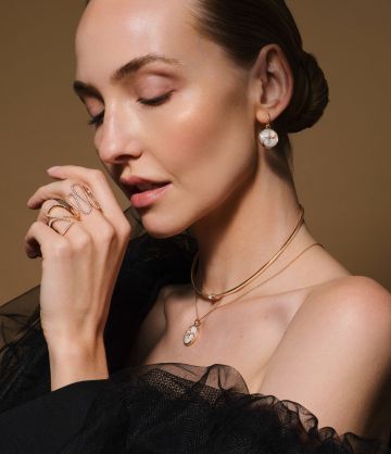 Zwei Frauen tragen Schmuck aus dem Atelier Mühlbacher: links Armreifen aus Gold und Diamant, rechts Goldringe, Halsketten und Perlmutt-Ohrringe in elegantem Licht.