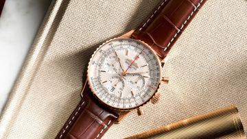 Breitling Navitimer Chronograph in Gold mit cremefarbenem Zifferblatt und braunem Lederarmband auf beigefarbenem Stoff liegend