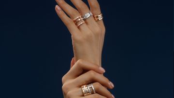 Damenhand vor blauem Hintergrund mit je einem Ice Cube Ring von Chopard an Zeige-, Mittel- und Ringfinger in Rosegold und Weissgold mit Diamanten