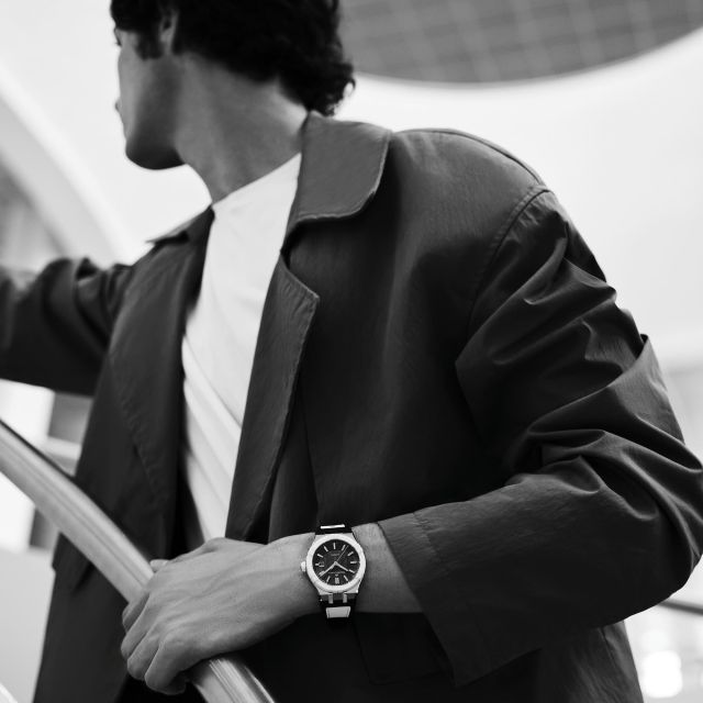 Mann in Jacke mit Maurice Lacroix AIKONIC Uhr, stilvolle Architekturkulisse, urbanes Lifestyle-Foto in Schwarz-Weiß.