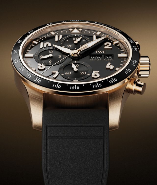 IWC Pilots Watch in Rotgold mit schwarzer Luenette, Zifferblatt und Kautschukarmband vor braungold-schwarzem Hintergrund
