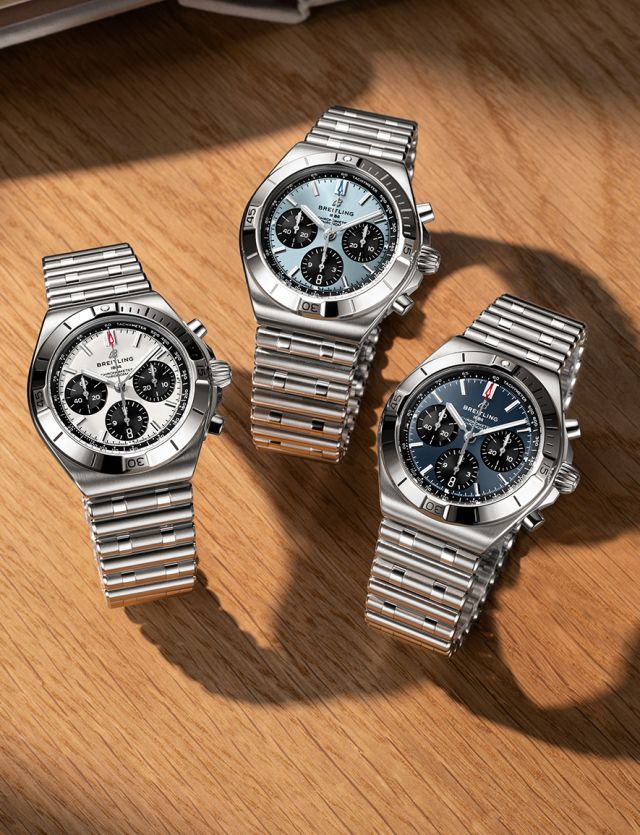 Drei Breitling Chronomat B01 42 Chronographen mit weißen, eisblauen und dunkelblauen Zifferblättern auf heller Holzoberfläche.
