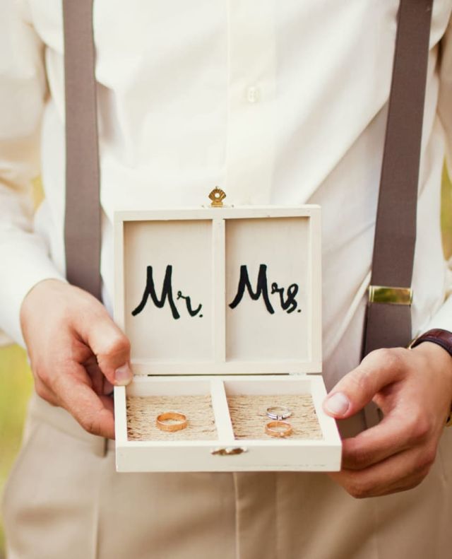Braeutigam haelt eine Holzbox in der Hand mit Aufschrift Mr und Mrs und den dazugehoerigen Eheringen