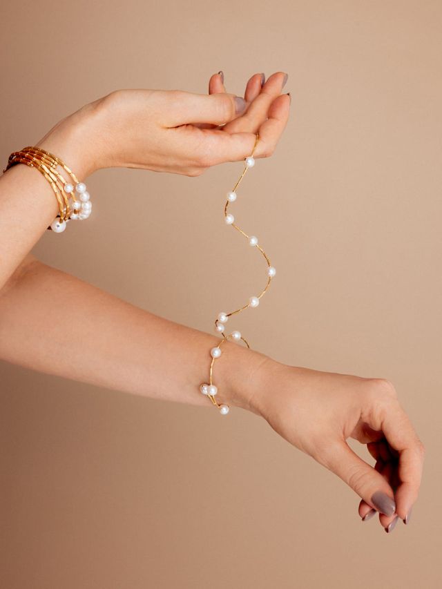 Nahaufnahme von Handgelenk mit Wickelarmband aus Gold und weißen Perlen, filigraner und eleganter Schmuck.