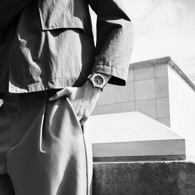 Mann mit Maurice Lacroix AIKONIC Automatikuhr am Handgelenk, modernes urbanes Outfit, stilvolle Schwarz-Weiß-Aufnahme.