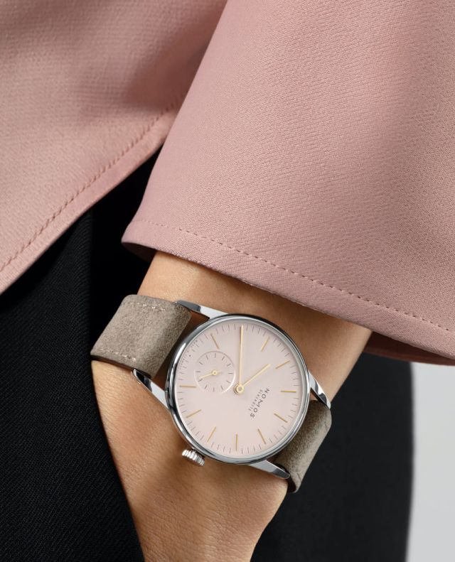 Weibliches Model mit NOMOS Glashuette Uhr in Stahl mit rosefarbenem Zifferblatt und Lederarmband am Handgelenk