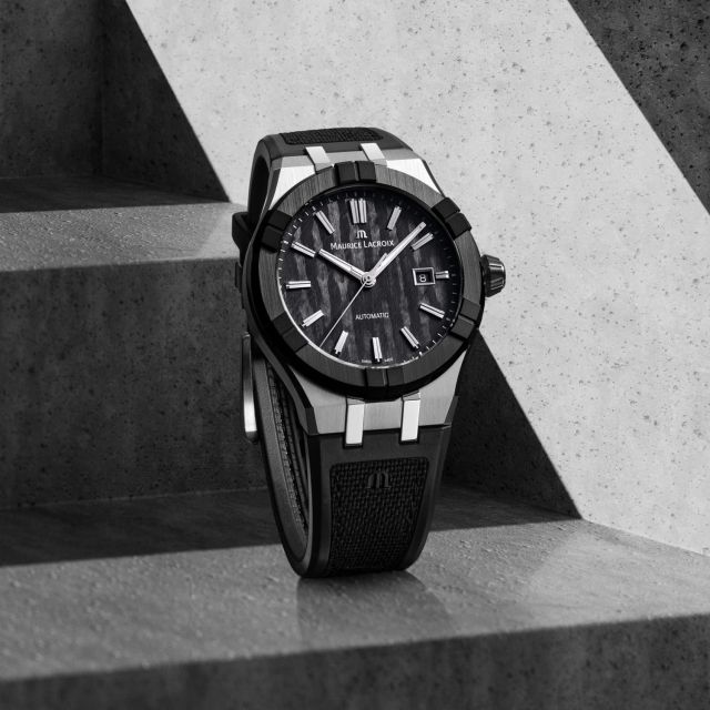 Maurice Lacroix AIKONIC Automatikuhr mit schwarzem Zifferblatt und Kautschukarmband auf Betontreppe, modernes Luxusuhren-Design.