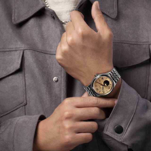 Lifestyle-Aufnahme: Jay Chou trägt eine TUDOR 1926 Luna mit champagnerfarbenem Zifferblatt und schwarzer Mondphasenanzeige zu grauer Jacke.