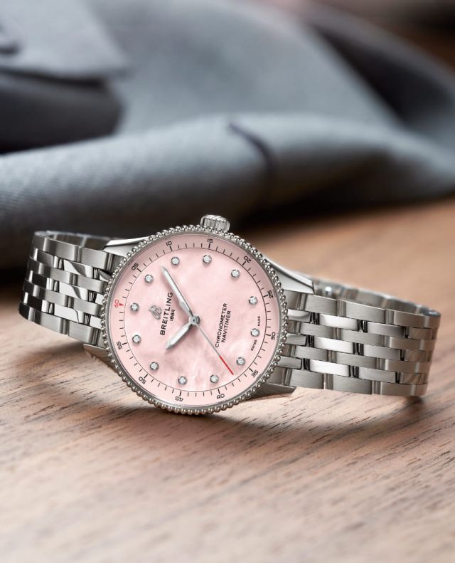 Breitling Navitimer Uhr in Stahl mit rosafarbenem Zifferblatt seitlich auf Holzuntergrund liegend