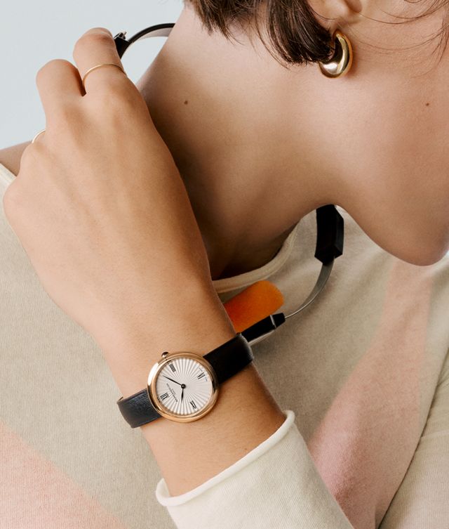 Baume & Mercier Joia Damenuhr mit roségoldfarbenem Gehäuse, weißem Zifferblatt und schwarzem Lederarmband am Handgelenk einer Frau