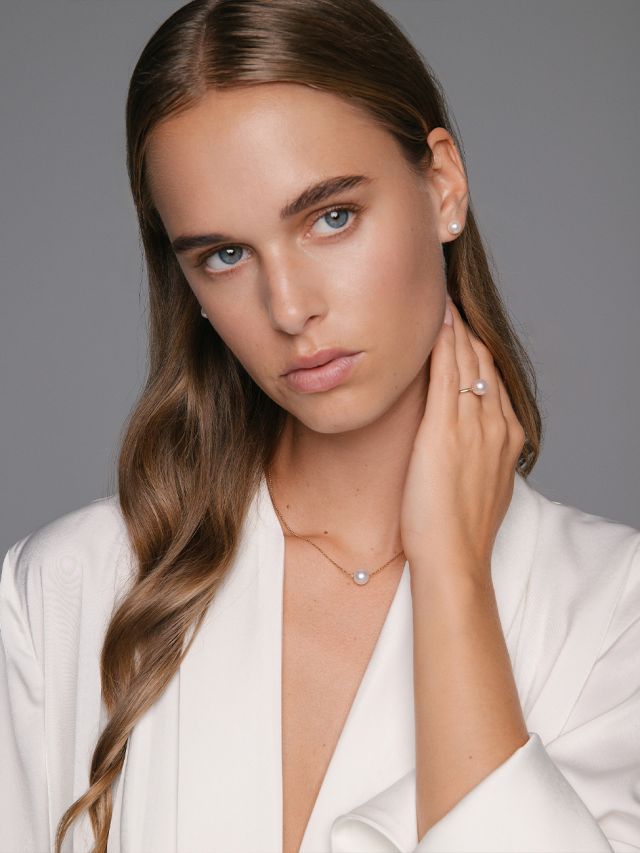 Weibliches Model tr&auml;gt Perlohrstecker, Perlring und Kette mit Perlanh&auml;nger aus der New Basics Kollektion von Yana Nesper.