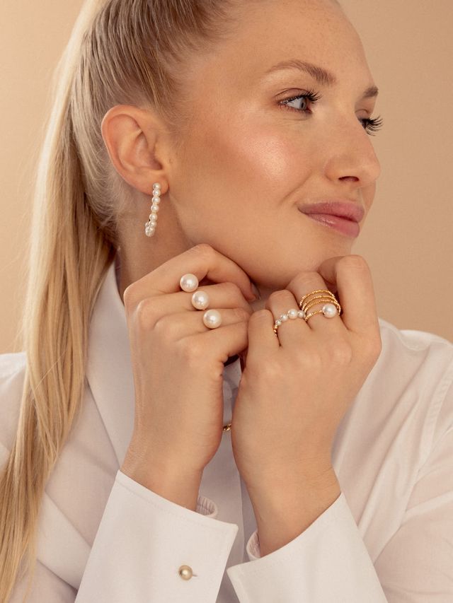 Blonde Frau mit eleganten Perlenringen und geschwungenen Perlenohrringen, klassische und luxuriöse Schmuckpräsentation.