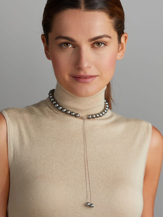 Frau mit schlichter Tahiti-Perlenkette in Y-Form, kombiniert mit beigem Rollkragenpullover, minimalistisch-eleganter Look.