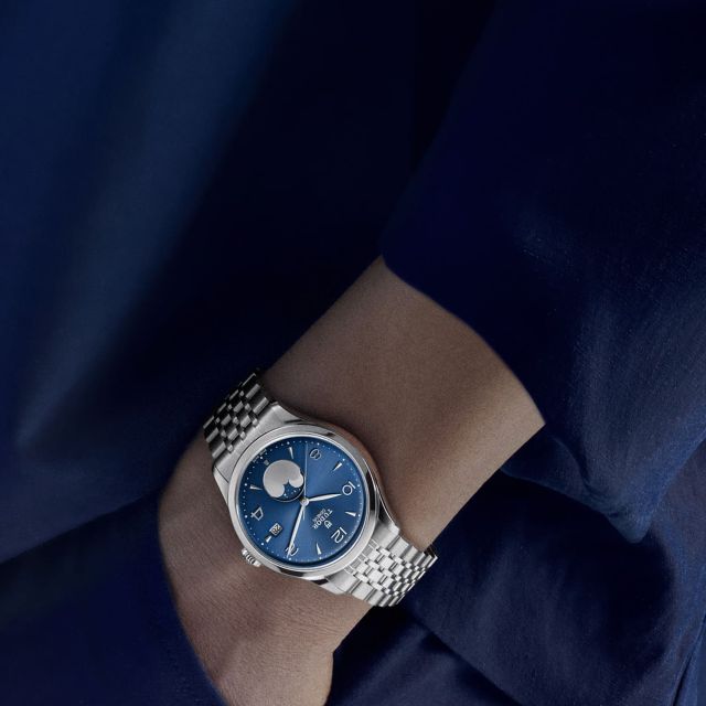 Die TUDOR 1926 Luna mit blauem Zifferblatt und Mondphasenanzeige am Handgelenk getragen, kombiniert mit dunkelblauer Kleidung.