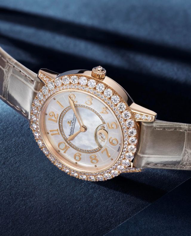 Jaeger-LeCoultre Rendez-Vous Uhr in Rosgold mit Diamantluenette und braunem Lederarmband seitlich auf blauem Untergrund liegend