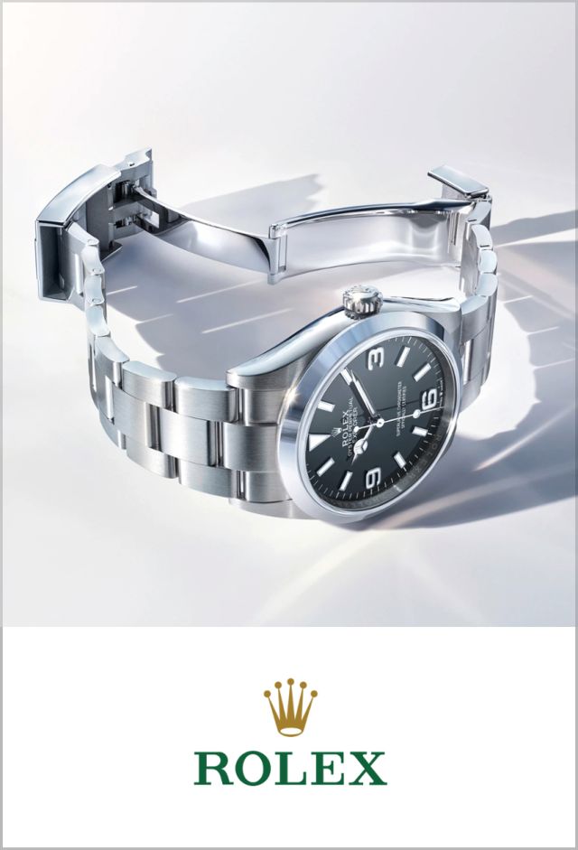 Rolex Logo unter Rolex Explorer 36 Ref. 124270 aus Oystersteel mit schwarzem Zifferblatt und Oyster-Band auf hellem Hintergrund