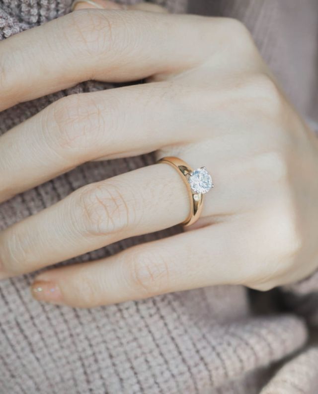 Damenhand mit Verlobungsring in Gelbgold mit einem Diamanten