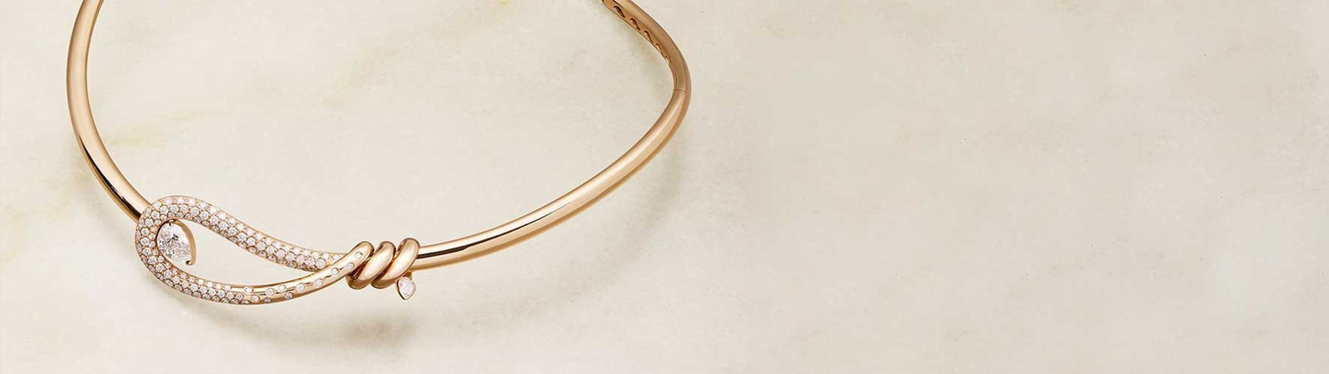 Ros&eacute;goldenes Collier aus der Closer Kollektion von Crivelli mit geschwungenem, diamantbesetztem Zierelement und feiner Knotenform, elegant inszeniert auf hellem Natursteinhintergrund