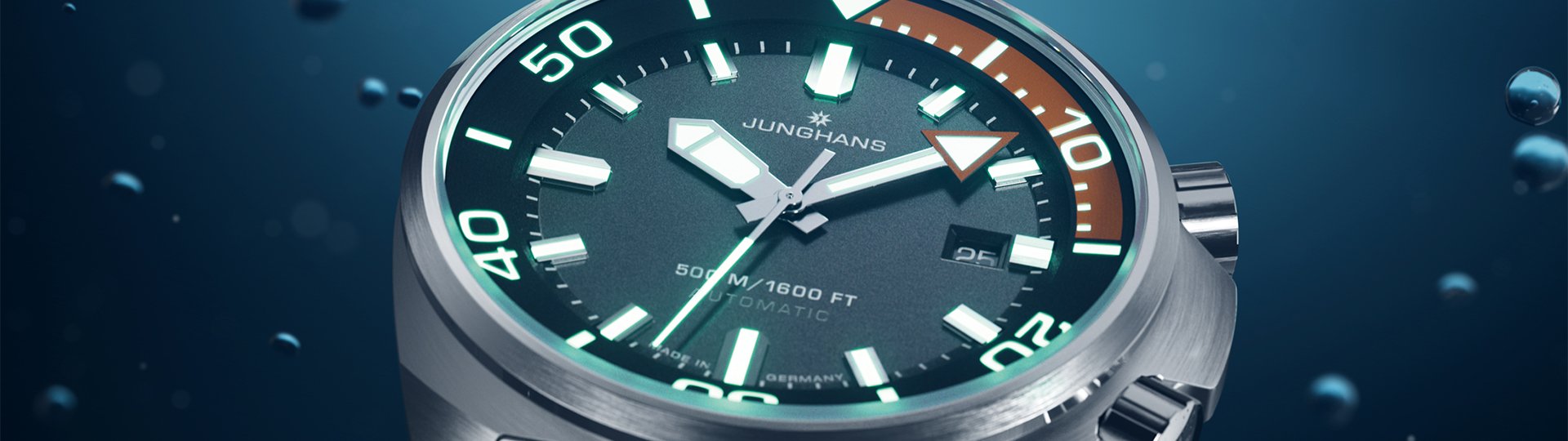 Detailaufnahme der Junghans Aquaris Diver Taucheruhr mit leuchtenden Indizes und orange markiertem Drehring vor Unterwasser-Hintergrund.